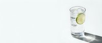 Refreshing glass of sparkling water with lime slice on white background casting shadow. Clean hydration concept for wellness and healthy lifestyle.