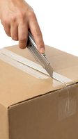 Male hand using utility knife to open cardboard shipping box on white background, isolated for delivery and logistics concepts.