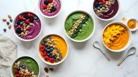 Colorful smoothie bowls with fresh berries, nuts and seeds arranged on white marble surface for healthy breakfast and nutrition lifestyle.