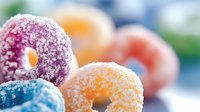 Colorful sugar-coated mini donuts in pastel pink, orange and blue tones on blurred background. Sweet dessert close-up with powdered sugar coating and soft focus.
