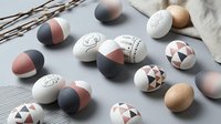 Modern Easter eggs with geometric patterns and minimalist designs in neutral colors scattered on white surface with willow branches.