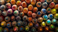 Colorful wooden pencils arranged in rows creating abstract pattern with vibrant tips showing wear and use, captured in dramatic lighting for artistic background.