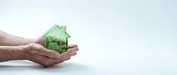 Hands holding green house model symbolizing eco-friendly real estate, sustainable living, property investment, and environmental responsibility concept.
