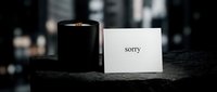 Elegant apology card with the word sorry beside a black candle on a dark stone surface, conveying sincere regret and emotional depth.