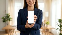 Professional Asian businesswoman in navy suit displaying blank smartphone screen in modern office workspace for mobile app presentation and digital marketing.