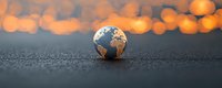 Small decorative globe on dark textured surface with warm bokeh lights in background creating magical atmosphere for environmental concepts.