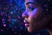 Young African American woman with glowing glitter makeup in profile against dark background with purple and blue sparkles creating magical atmosphere.