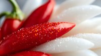 Fresh red chili peppers with water droplets in macro photography against white background, showing vibrant color and texture detail for culinary design.