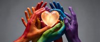 Diverse hands painted in rainbow colors holding glowing heart symbol together, representing unity, love, inclusion, and community support for charitable causes and social movements.