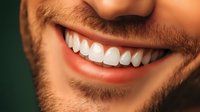 Close up of bright white healthy smile showing perfect teeth and trimmed beard on male face against dark background. Dental care concept.