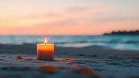 Glowing orange candle on sandy beach at sunset, with blurred ocean waves and warm sky in background creating peaceful seaside atmosphere.