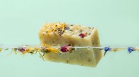 Natural handmade soap bars with dried flowers floating in clear water against mint green background for spa and wellness concepts.