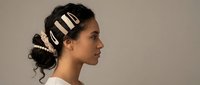Young mixed-race woman in profile with elegant pearl and nude hair clips styling dark updo hair, neutral background, beauty fashion concept.