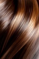 Smooth brown hair with highlights showing glossy, healthy texture and shine. Close-up macro shot reveals natural wave pattern and dimensional color tones.
