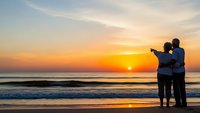 Romantic couple silhouettes embracing on beach at golden sunset with ocean waves and colorful sky for travel and love concepts.
