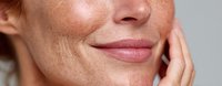 Close-up of woman's face with freckles, showing natural skin texture and gentle smile, hand touching cheek in skincare or beauty concept.