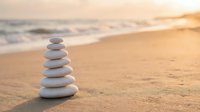 Balanced stack of smooth white stones on sandy beach at golden sunset with ocean waves creating peaceful zen meditation scene for wellness and mindfulness.