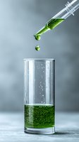 Green liquid drops falling from syringe into glass beaker with bubbling solution against gray background, capturing moment of scientific experiment.