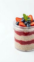 Chia seed pudding with fresh strawberries and blueberries in glass jar topped with mint leaf on white background for healthy breakfast recipes.
