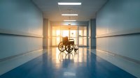 Empty wheelchair in bright hospital corridor with sunlight streaming through windows creating warm glow on polished floors for healthcare concepts.