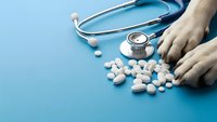 Dog paws with scattered white pills and stethoscope on blue background representing veterinary medicine and pet healthcare treatment.