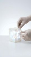 Gloved hands assembling transparent geometric cube structure on white background, representing laboratory research, scientific innovation, and biotechnology development.