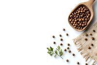 Aromatic allspice peppercorns scattered from wooden spoon with fresh herbs and natural burlap on white background, food photography styling composition.