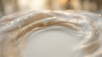 Creamy white liquid swirl with water droplets, soft golden bokeh background, luxurious texture for skincare, cosmetic, or food product concepts.