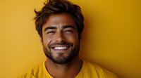 Young Latino man with beard and trendy hairstyle wearing yellow t-shirt smiling genuinely against yellow background, showing white teeth and positive attitude.