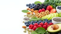 Colorful superfood collection with fresh berries, nuts, seeds and avocado arranged on white background for healthy eating and nutrition concepts.