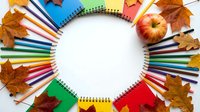 Back to school concept with colorful pencils, notebooks, apple and autumn leaves arranged in circle on white background for educational design.