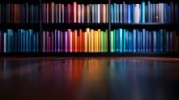 Colorful book spines arranged in rainbow order on wooden shelves create vibrant reflections on glossy surface, dramatic lighting enhances spectrum display in library setting.