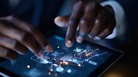 African American businessman hands working on futuristic digital tablet interface with glowing circuit patterns and technology elements in dark office setting.