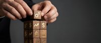 Businessman hands stacking wooden blocks with financial symbols including dollar signs and growth charts representing investment strategy and wealth building.