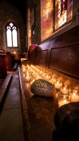 Church interior with glowing candles and Give Hope stone message creating peaceful spiritual atmosphere with warm light through stained glass windows.