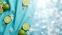 Fresh lime slices and white flowers on turquoise fabric background with soft bokeh lights creating tropical summer atmosphere for spa and wellness concepts.