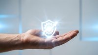 Caucasian male hand holding glowing shield icon symbolizing data protection, cybersecurity, and digital safety for business and technology concepts.