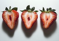 Fresh strawberry halves showing juicy red flesh and green leaves arranged in a row on white background, perfect for food packaging and recipe designs.