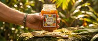 Beekeeper holding jar of raw honey with wooden dipper against blurred garden foliage, showcasing natural organic product for food and wellness packaging.