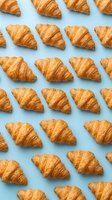Golden croissants arranged in repeating rows on light blue background, creating seamless pattern for bakery, food, and breakfast design projects.