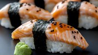 Fresh salmon nigiri sushi with black sesame seeds and wasabi paste on dark background, selective focus on raw fish slices atop white rice wrapped in nori.