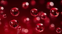 Red soap bubbles floating against blurred crimson background with bokeh lights creating festive atmosphere for holiday decorations and romantic designs.