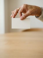Senior woman with aged skin holding blank white card in hand, displaying mockup space for text or branding on wooden surface background.