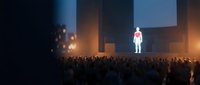 Business speaker presenting to large audience in modern conference hall with dramatic stage lighting and corporate atmosphere.