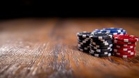 Stacked poker chips in black, blue and red on rustic wooden table with dramatic lighting and shallow depth of field, creating atmospheric gambling scene.