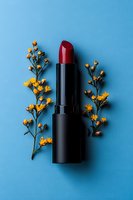 Red lipstick with yellow wildflowers arranged on bright blue background. Minimalist beauty and cosmetics flat lay composition for advertising and design.