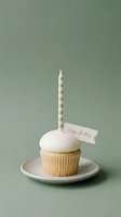 Vanilla cupcake with white frosting, striped candle and happy birthday tag on a plate, sage green background, minimalist celebration concept.