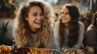 Young blonde and brunette women laughing while enjoying fresh fruit and snacks outdoors on sunny day, genuine friendship and joyful lifestyle moment captured.