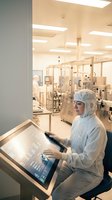 Scientist in protective cleanroom suit operating touchscreen computer in sterile pharmaceutical laboratory environment for research and development.