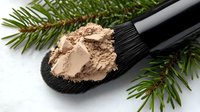 Natural mineral makeup powder on black brush with evergreen spruce branches for organic cosmetics and beauty products.